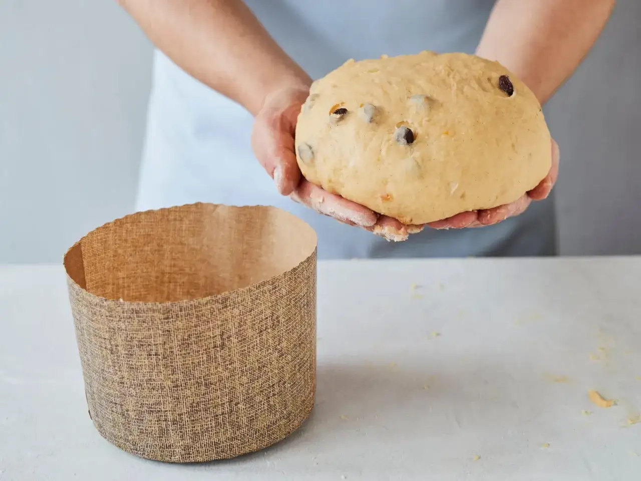 H&auml;nde halten einen Teig f&uuml;r ein Panettone Rezept, daneben steht eine leere Backform.