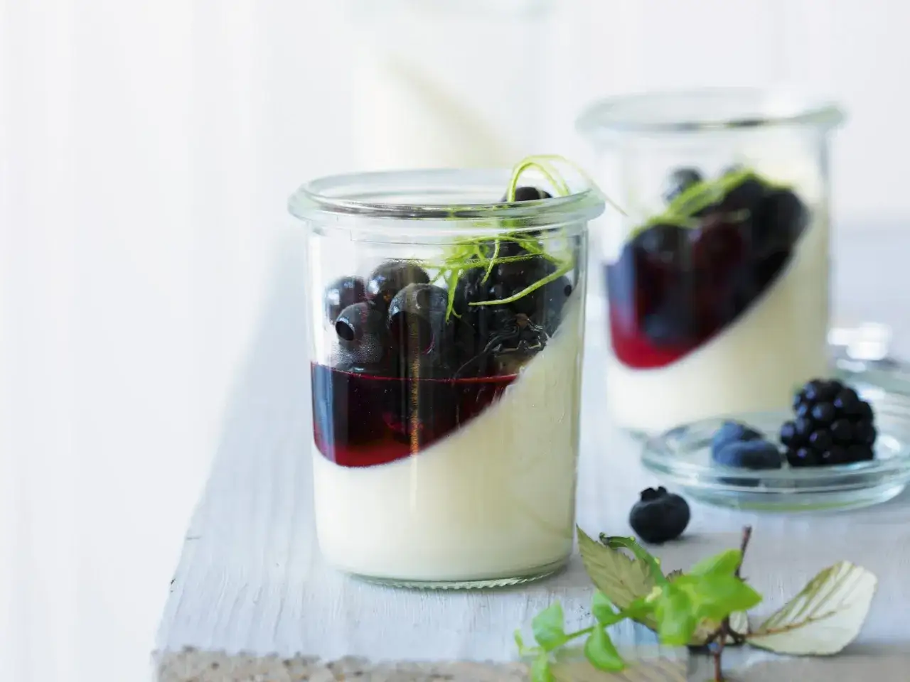 Zwei Gläser Panna Cotta mit Blaubeeren und einem Hauch von Limette. Ein köstlicher Genuss!