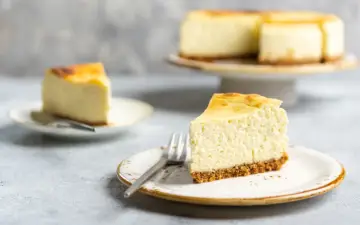 Ein cremiger Kuchen mit Mascarpone, auf einem Teller mit Gabel, daneben ein weiteres Stück und ein ganzer Kuchen.
