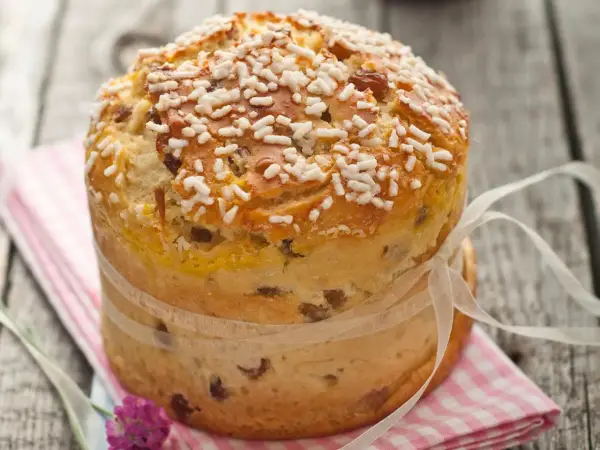 Ein goldbrauner Panettone mit Rosinen und Zuckerkristallen, gebunden mit einem Satinband. Ein köstliches Panettone Rezept zum Nachbacken.