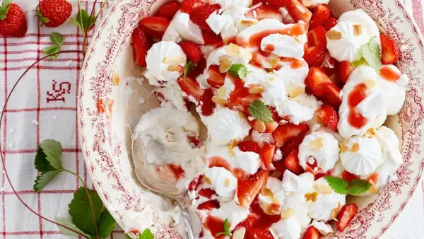 Ein köstlicher Eton Mess mit frischen Erdbeeren, Baiser und Sahne, garniert mit Mandelsplittern und Minze.