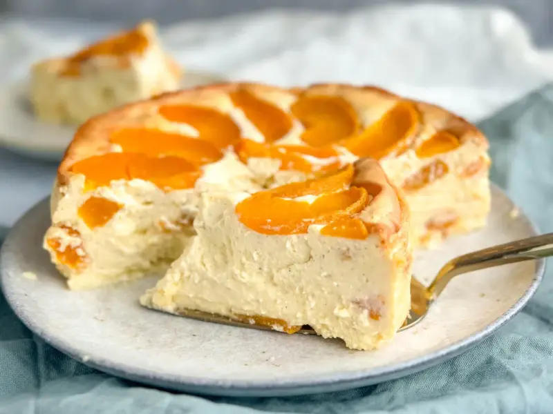 Ein saftiger Pfirsichkuchen mit cremiger Füllung und frischen Pfirsichspalten. Ein Stück wird gerade mit einem goldenen Tortenheber herausgehoben.