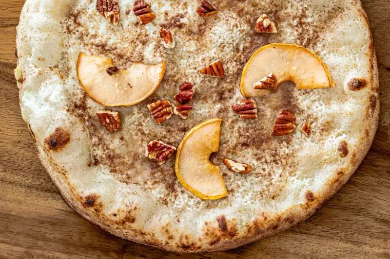Eine süße Pizza mit dünnem Teig, bestreut mit Zimt, belegt mit Apfelscheiben und Pekannüssen. Ein Genuss wie eine Nutella Pizza!