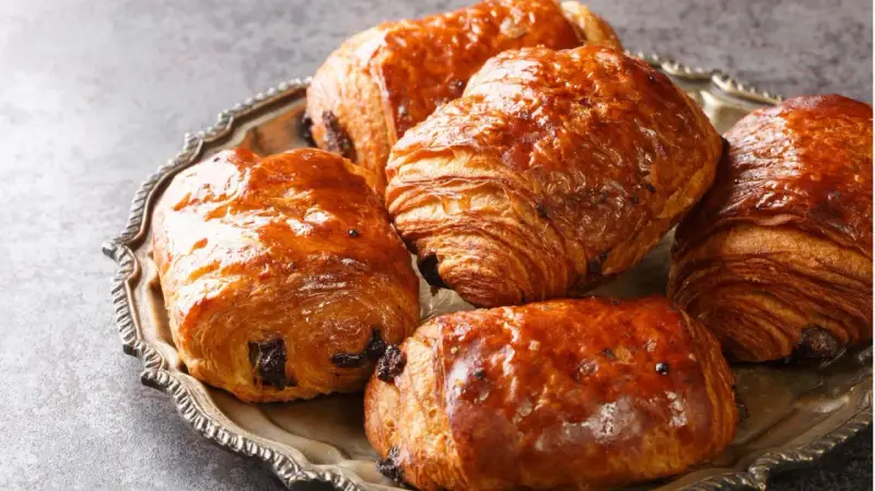 Einige goldbraune, knusprige Pain au Chocolat liegen auf einer silbernen Platte.