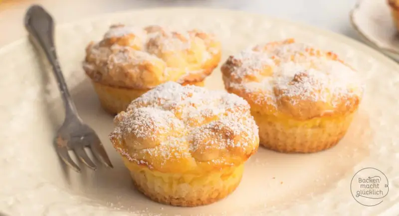 Drei luftige cheesecake muffins, bestäubt mit Puderzucker, warten auf einer Platte auf eine Gabel.