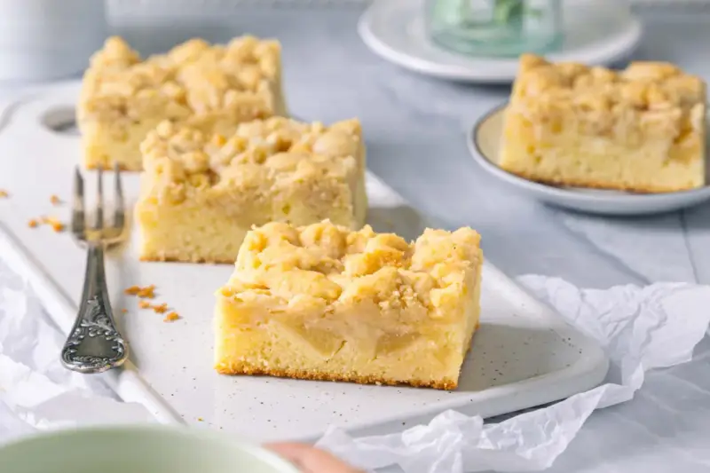 Saftiger Apfelkuchen mit Streuseln, perfekt für eine Kaffeepause. Ein Stück ist schon auf einer kleinen Platte angerichtet.