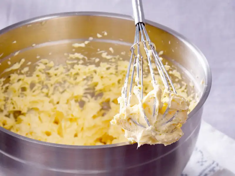 Ein Schneebesen mit cremigem Teig, bereit für ein Buttercreme Rezept.