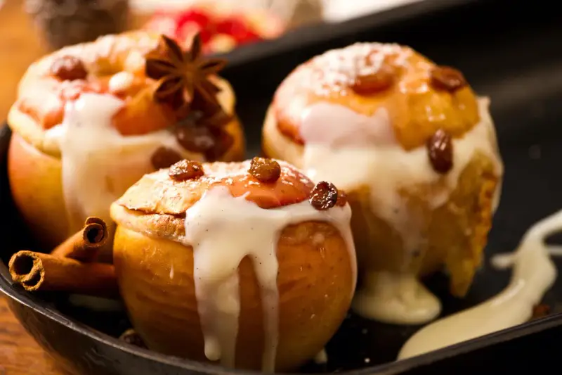 Drei köstliche Bratäpfel, übergossen mit Vanillesauce und garniert mit Rosinen und Zimtstangen. Ein perfektes Bratapfel Rezept für kalte Tage.