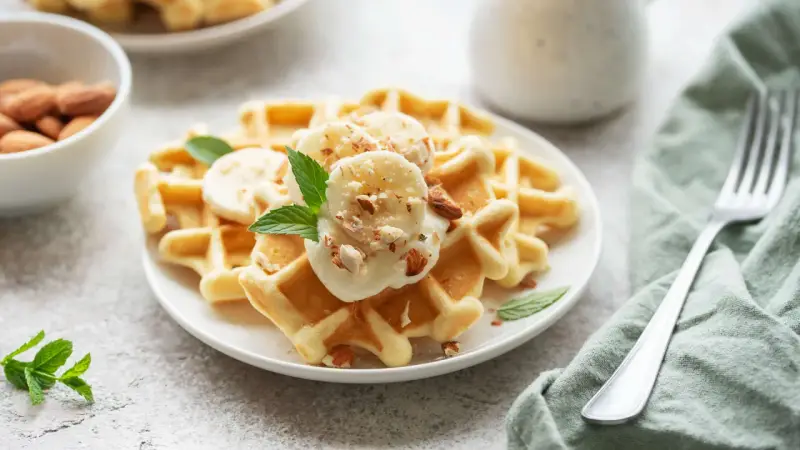 Goldbraune Skyr Waffeln mit Bananenscheiben, gehackten Mandeln und Minze. Ein köstlicher Start in den Tag!